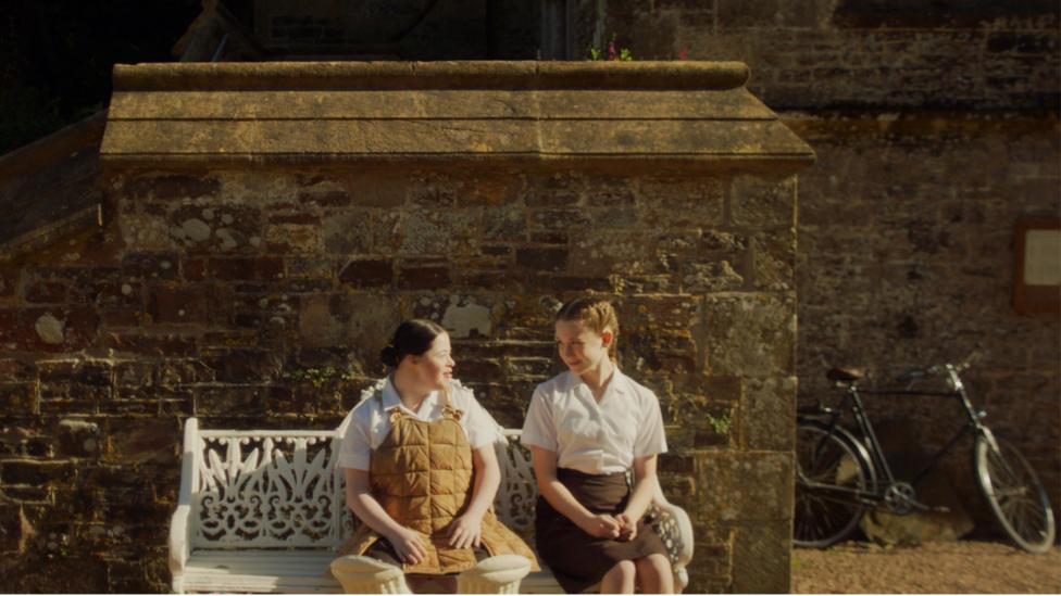 Nancy and Clarissa from Malory Towers sit on a bench outside