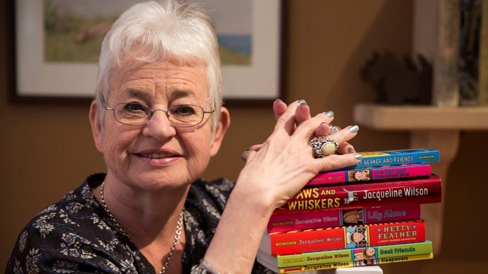 An old lady with short gray hair standing next to the children's books she's written