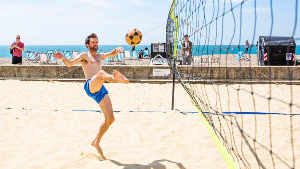 A man volleys a ball in the air playing footvolley on the beach.