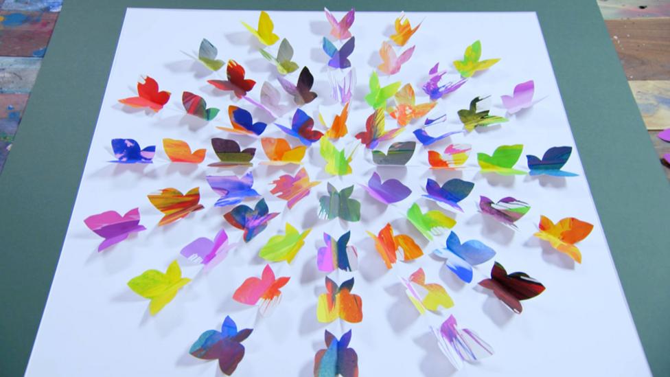 Colourful paper butterflies stuck to a piece of paper.