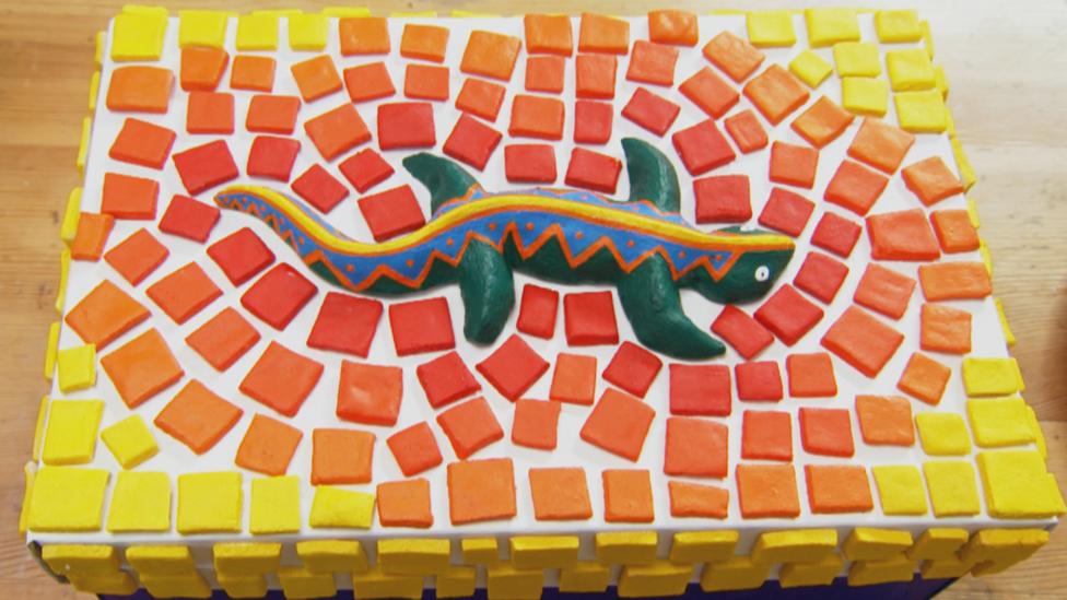 A green lizard on a mosiac box.