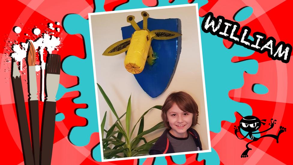 A boy (William) smiles beneath a giraffe head shield on the wall.