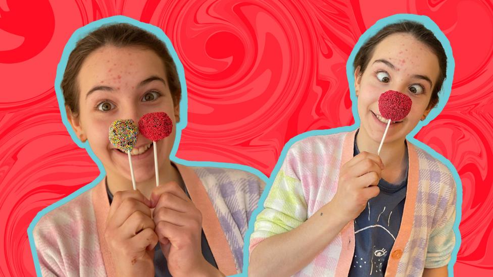 Junior Bake Off's Amelia holds two Red Nose Day Cake pops up to her nose and pulls a silly face.