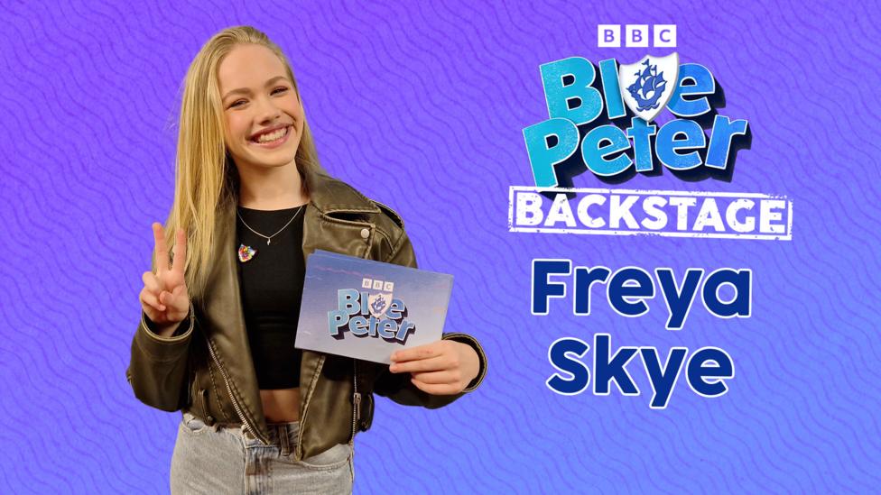 Freya Skye poses and smiles and holds up some Blue Peter branded cards.