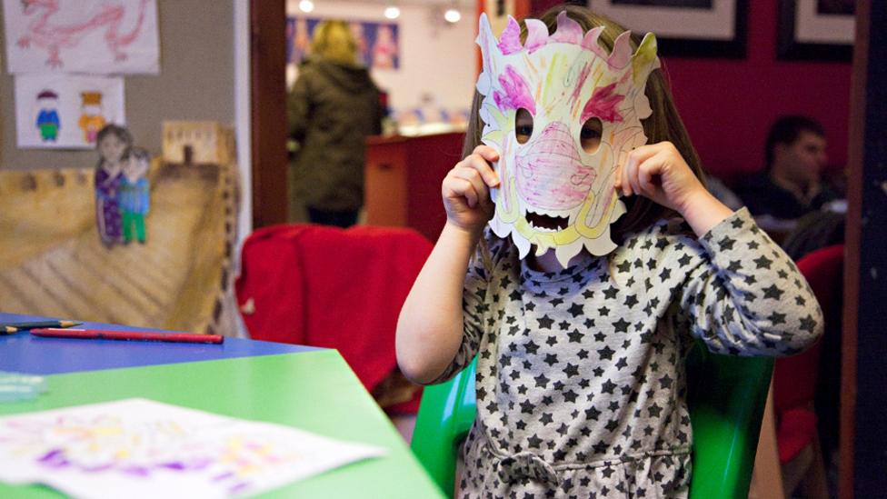 A young girl wearing a dragon mask she coloured in