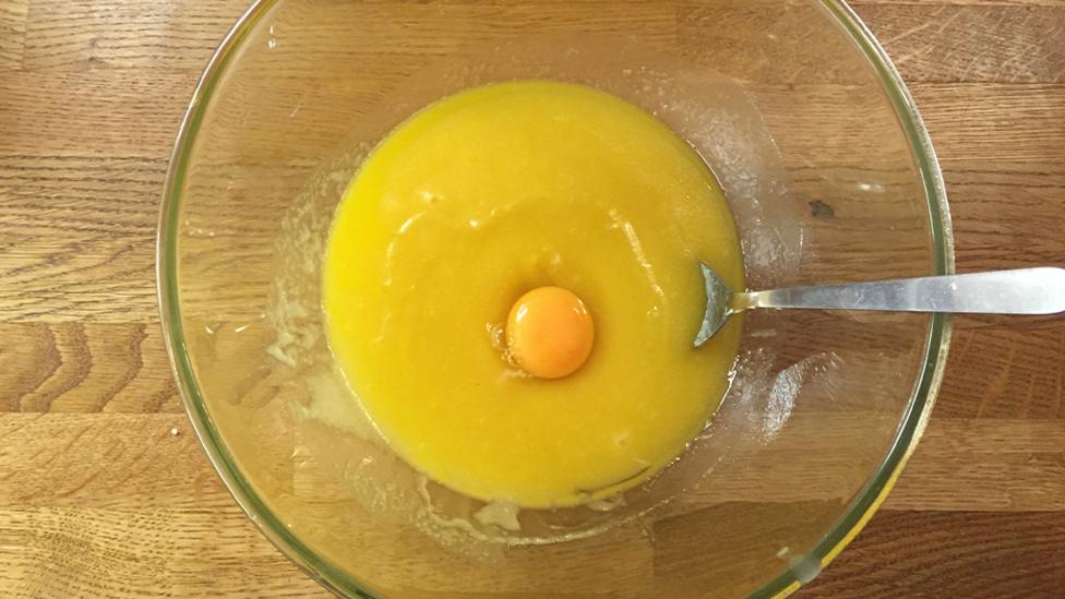 Beating an egg into a mixture of butter, sugar and vanilla extract.