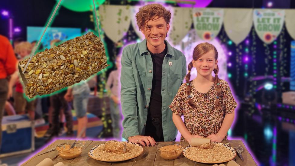 Joel and a young girl smile in front of an easy to make bird feeder, they are in the Blue Peter studio with lots of lights.