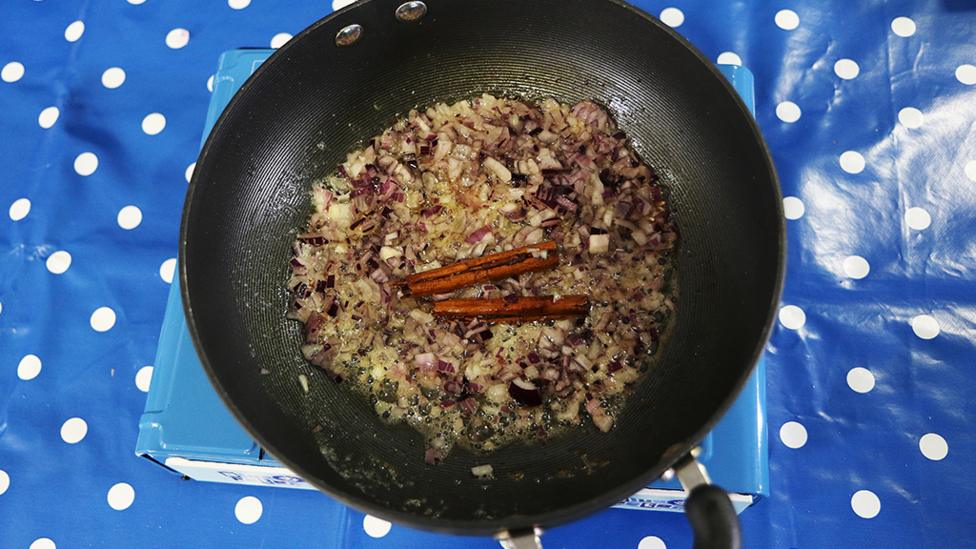 Cinnamon sticks and onions in a pan.