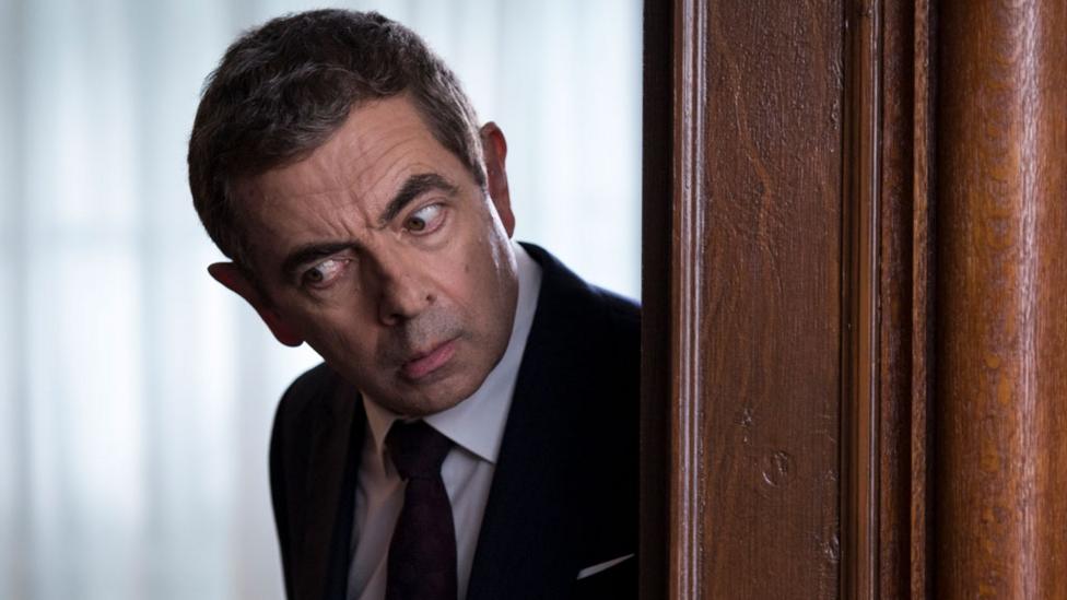 Johnny English peering around a door.