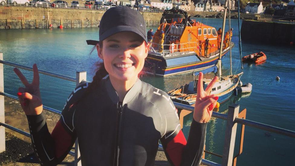 Lindsey in a wet suit in front of a lifeboat