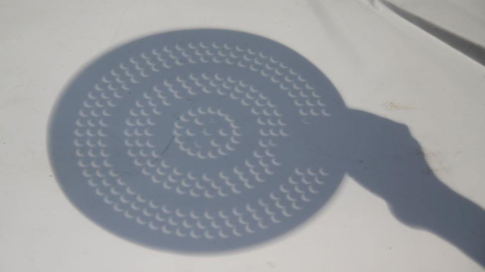 A colander full of holes is projecting the image of the sun during a solar eclipse.