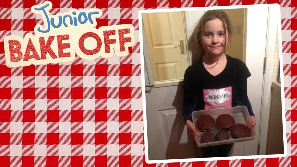 A girl holding a box full of red velvet whoopie pies.