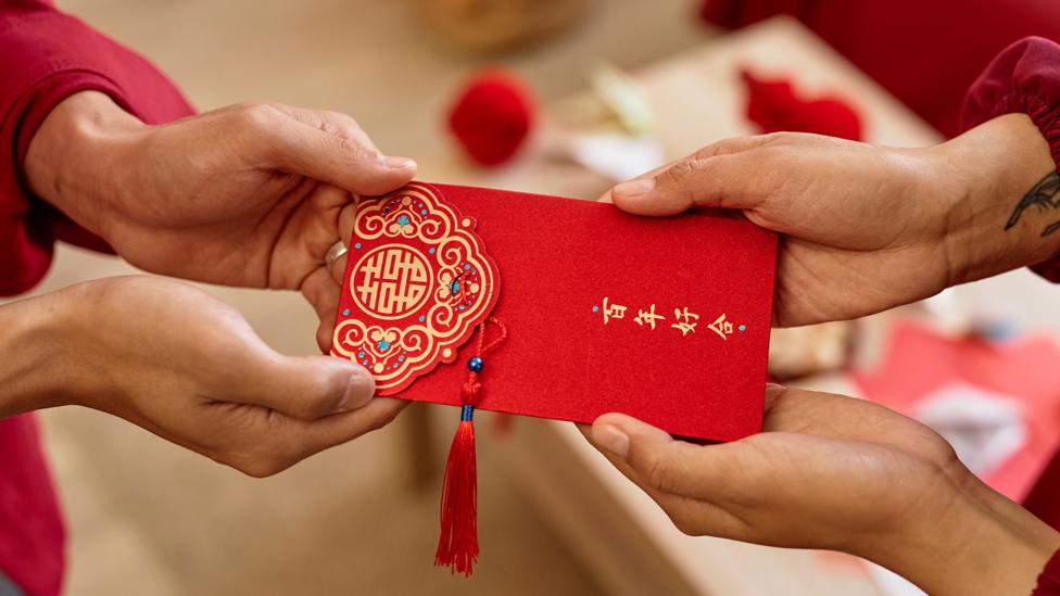 Two people holding a red envelope