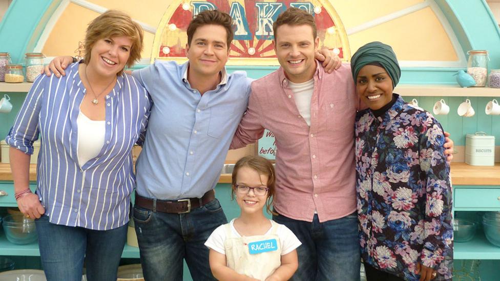 A young girl called Rachel stands in the Bake Off tent with judges Allegra and Nadiya and Sam and Mark.