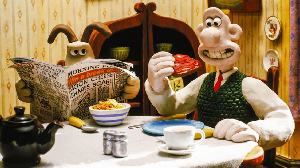 Wallace and Gromit are sitting at a dining table eating food
