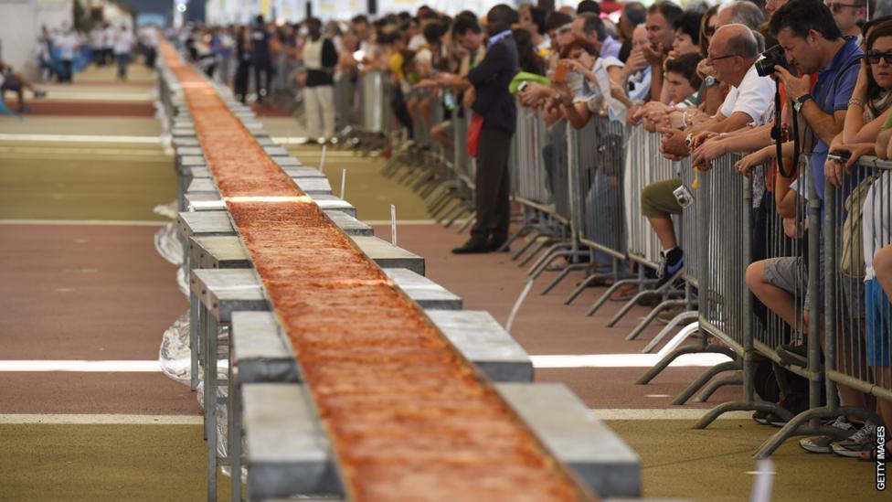 A long pizza with a crowd of people.