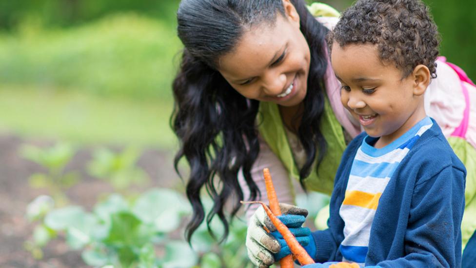 Little boy with his mother in the garden looking happy. The little boy is holding a carrot