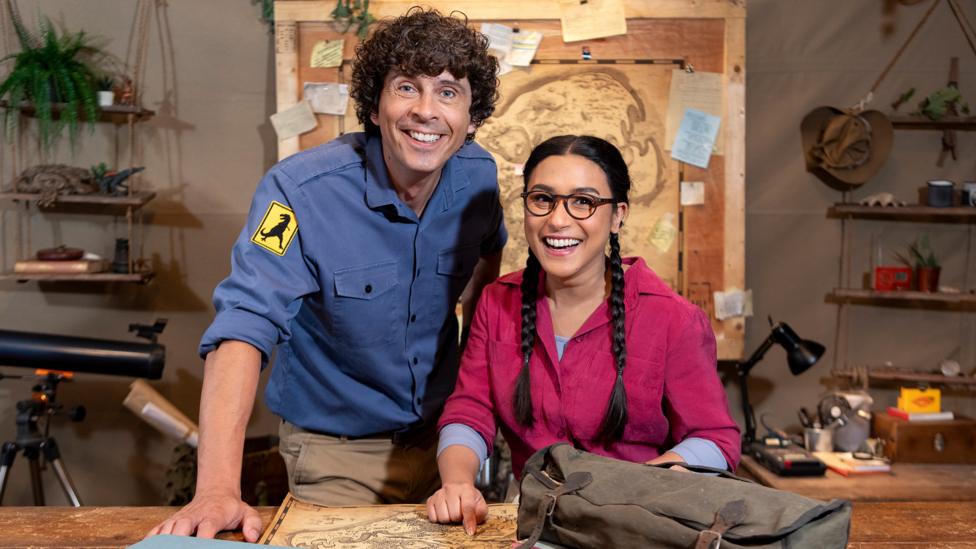Image of Andy and Jen smiling at the camera with an old map in the background and exploration kit.