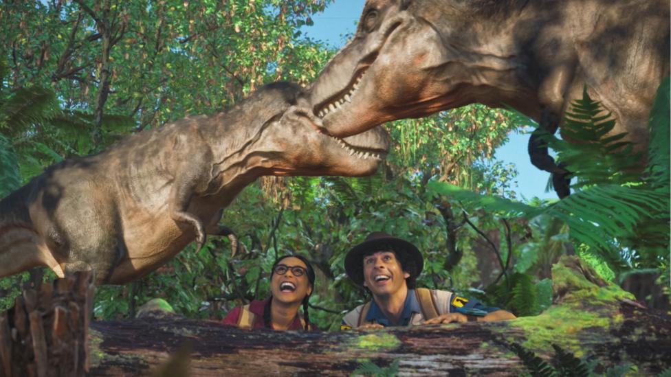 Andy and Jen are crouching in the jungle and looking up at two dinosaurs towering above them.