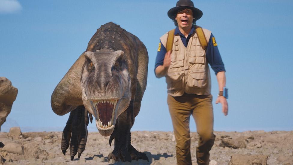 Andy is running from a dinosaur who is chasing him in a desert.