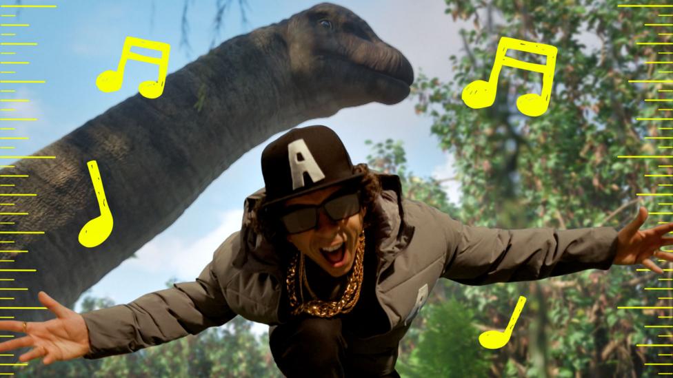 Andy Day in cap, sunglasses and gold chains rapping, with large dinosaur behind him.