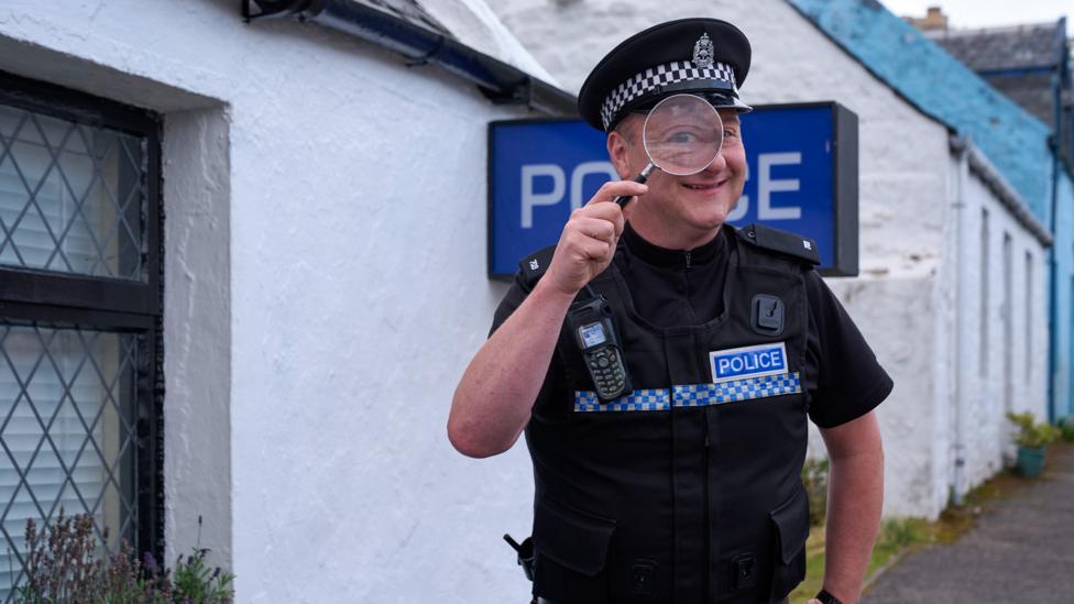 PC Plum looks through a microscope stood outside the Police station