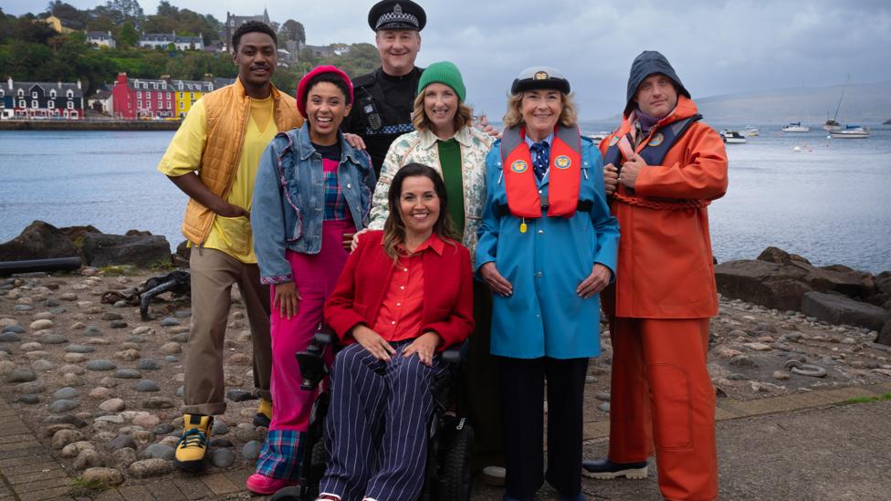 Image of a group of people dressed in bright colours stood by the harbour in Balamory.