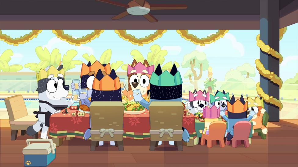 Bluey and her friends and family are gathered around a table wearing party hats