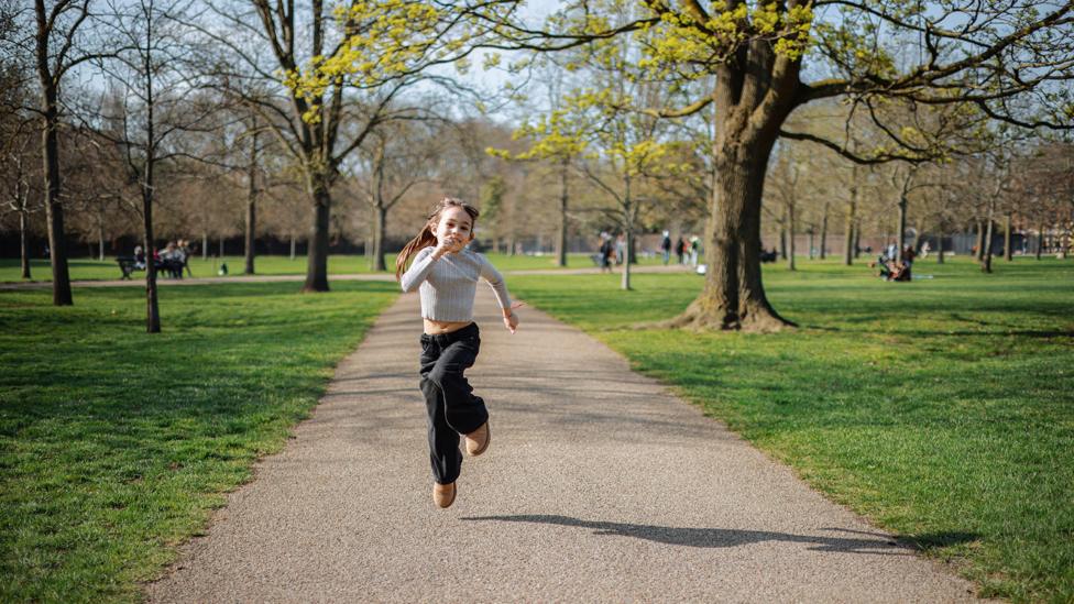 Image of a girl running along a path in the middle of a park.