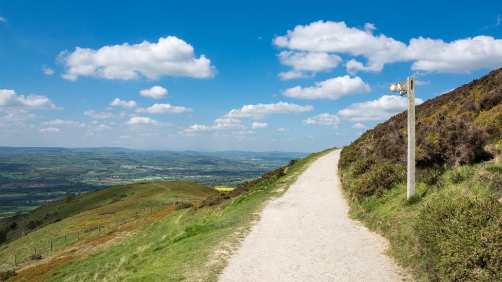 Image of a mountain with a path on the right side and a cloudy blue sky.