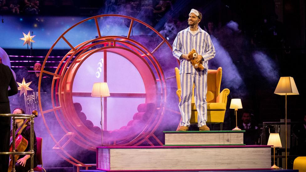 CBeebies Prom storyteller Joel Dommett in blue and white striped pyjamas, but the CBeebies chair, ready to start the show.