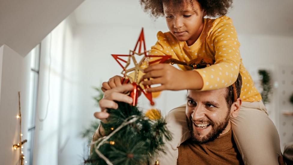 ather and daughter decorating a Christmas tree for the New Year and Christmas holiday.