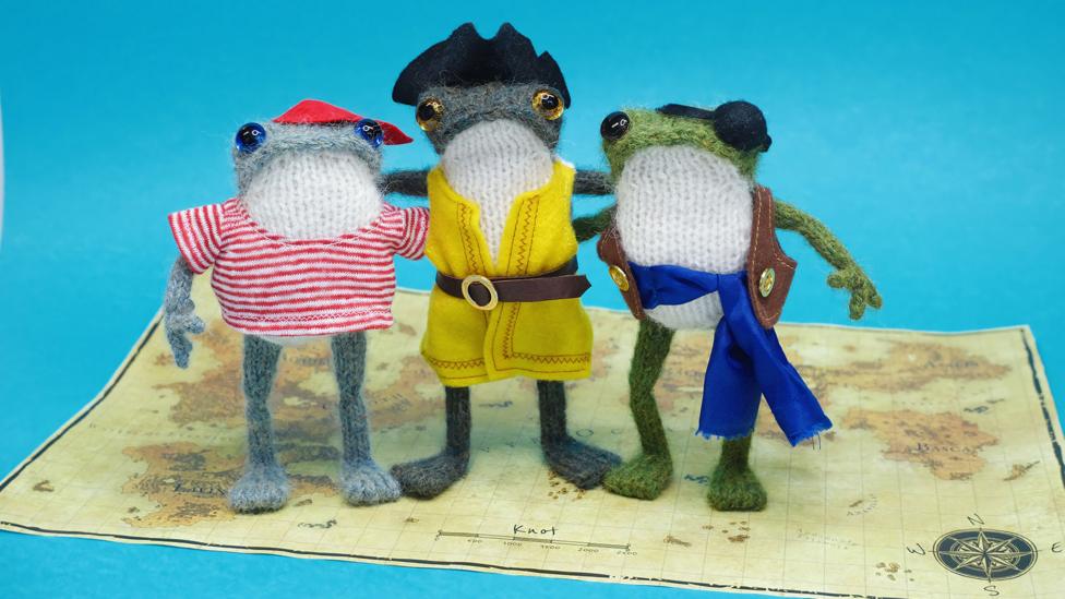The knitted frog trio are dressed as high seas pirates, standing on a treasure map.