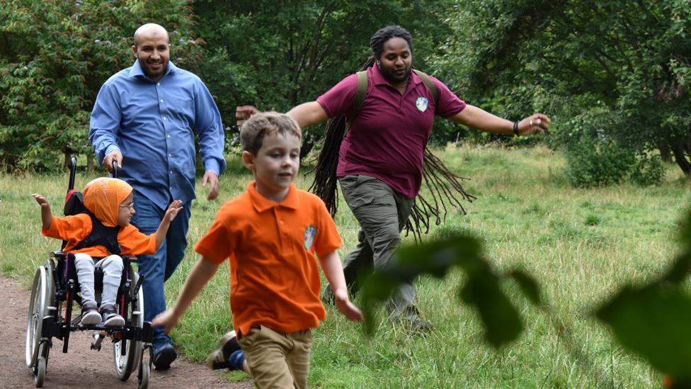 Image of children and adults walking through a forest with Ranger Hamza.