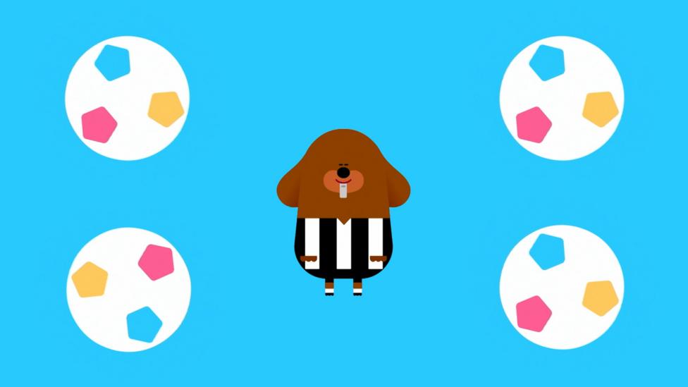 Duggee is dressed in an referee outfit with a blue background surrounded by footballs.