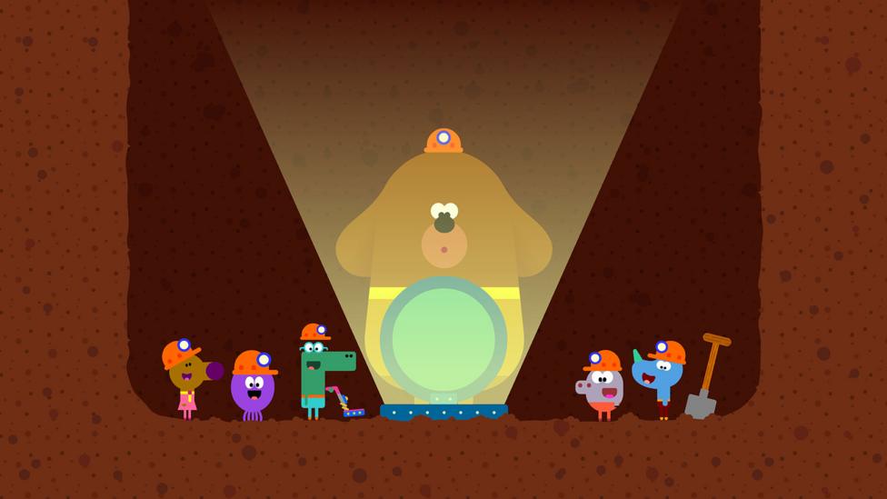 Cartoon dog Duggee standing in a dirt tunnel with the Squirrel Club, staring in wonder into an open hatch.