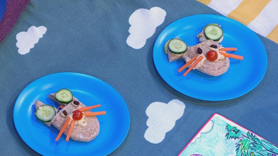 A blue plate holding mouse faces made from wholewheat pitta bread, carrot sticks for whiskers and cucumber for ears.