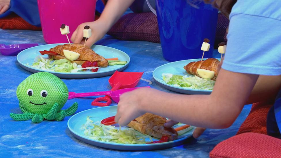 Children making croissant crabs, with red pepper claws and cheesy smiles.