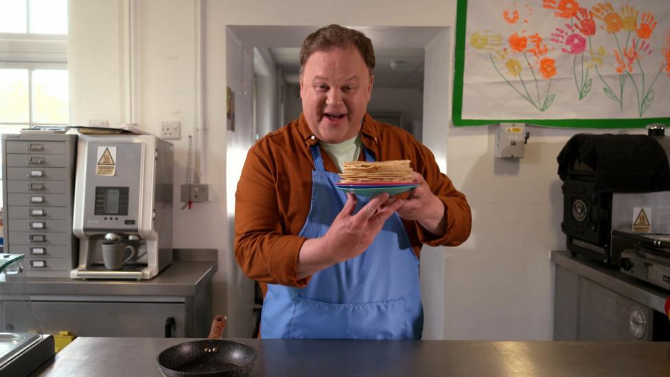Justin holding a plate of pancakes in a kitchen