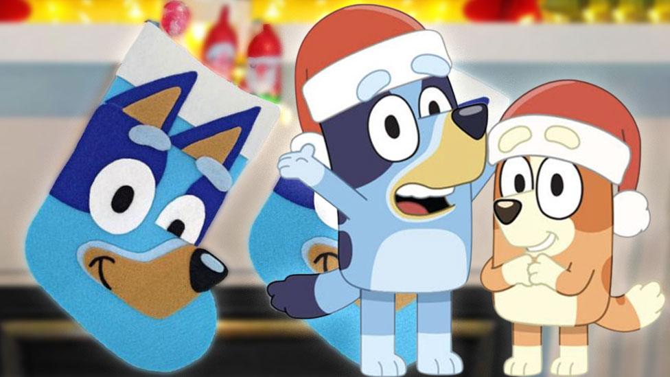 Bluey and Bingo in santa hats, smiling, next to a DIY felt Bluey stocking.