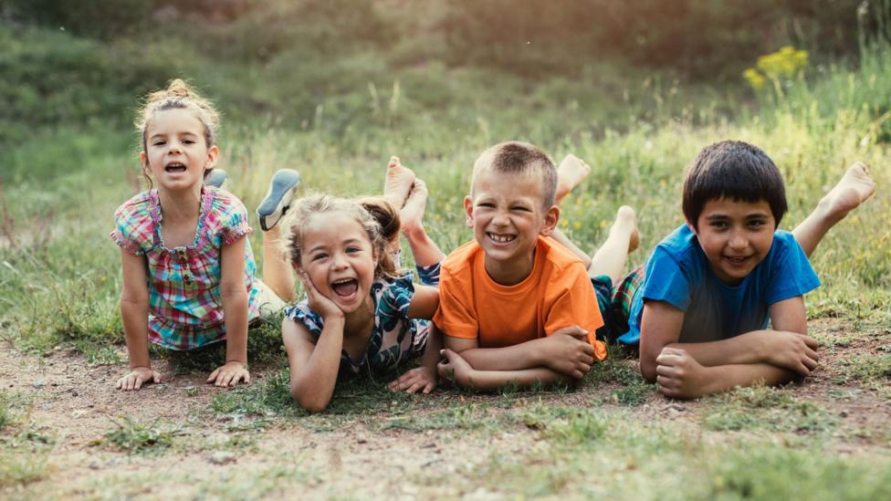 Four young children lying on the floor facing forward looking happy.