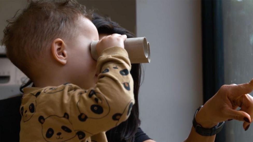 A child uses cardboard tubes as binoculars with his mum.