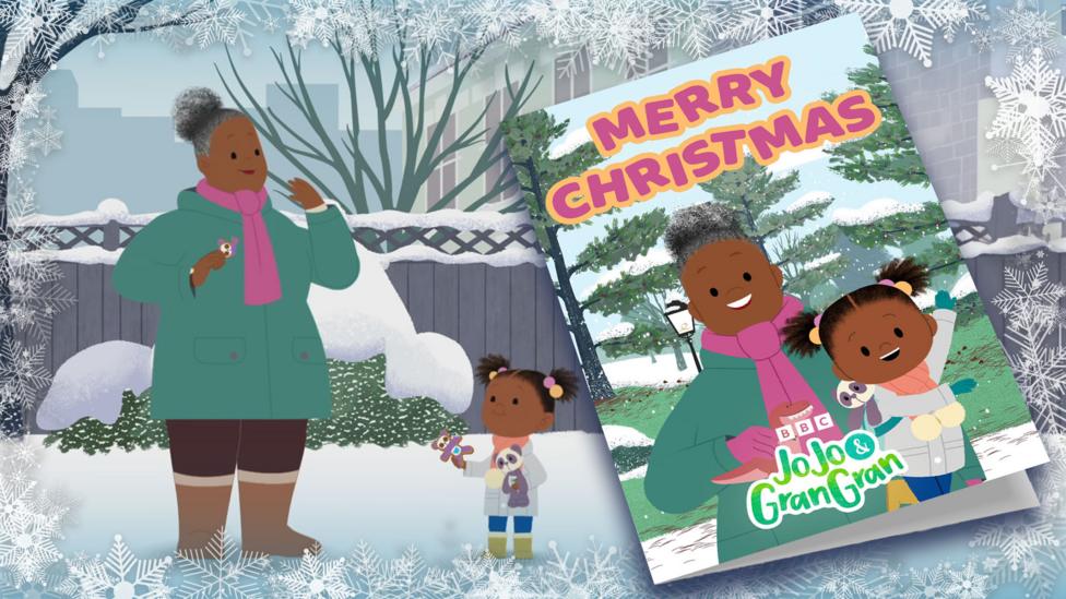 JoJo and Gran Gran standing in the snow, eating gingerbread biscuits, next to a giant Christmas card template.