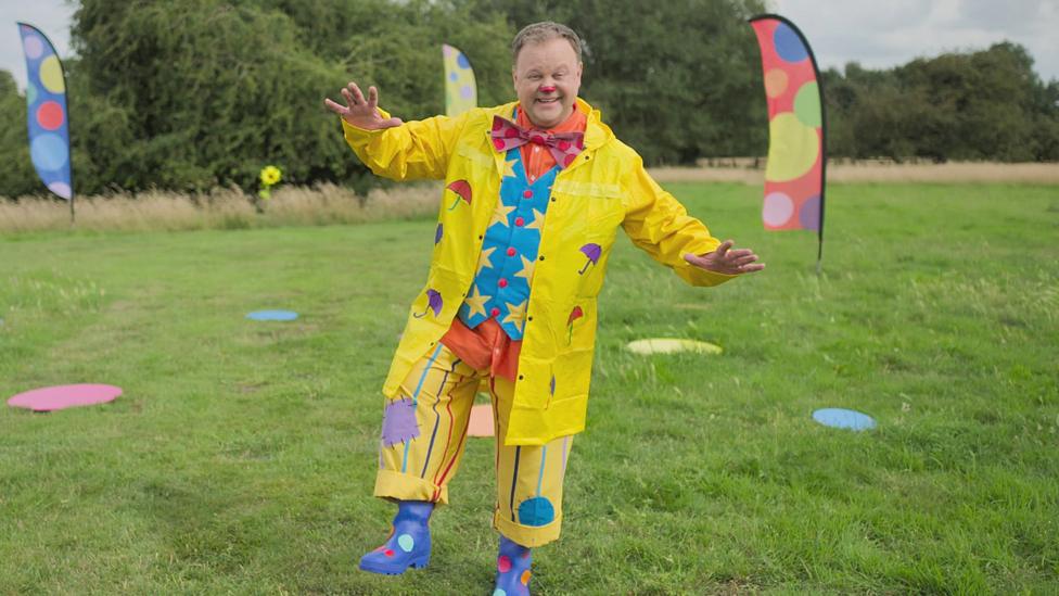 Mr Tumble from Something Special wearing a yellow jacket and wellies in a field