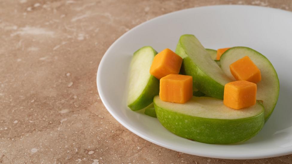 Green apple sliced with orange cubes of cheese on a white plate.