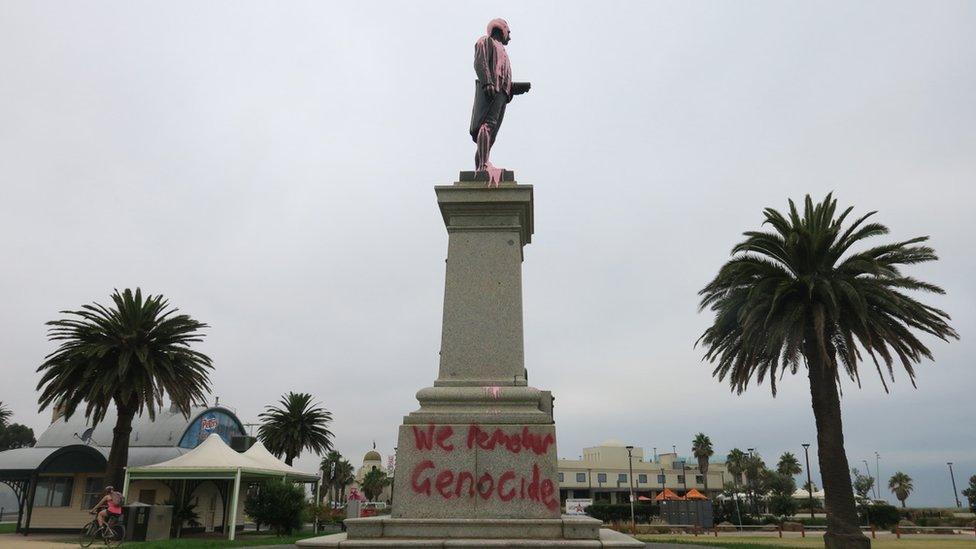 A statue of Captain Cook covered in pink paint and spray-painted with the words: "We remember genocide"