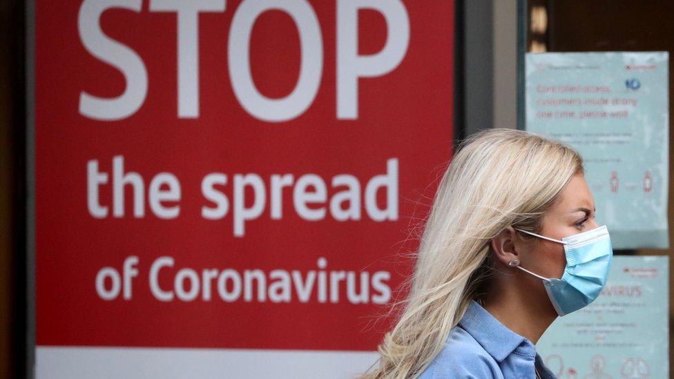 A woman wearing a mask walks past a sign that reads: Stop the spread of coronavirus