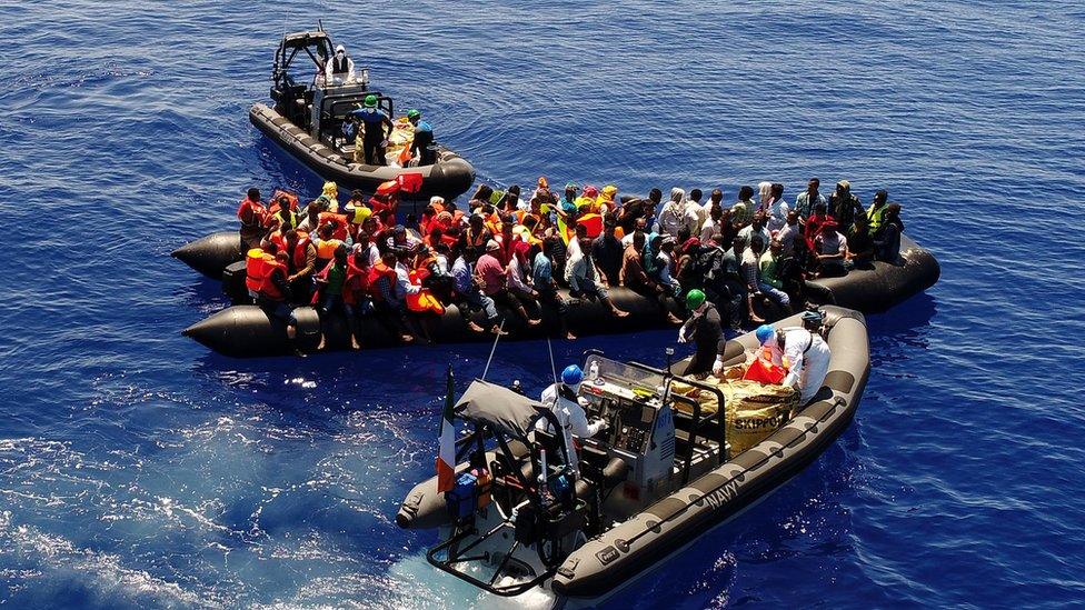 Small boats are pictured attending to migrants on top of an inflatable boat they are loaded on to.