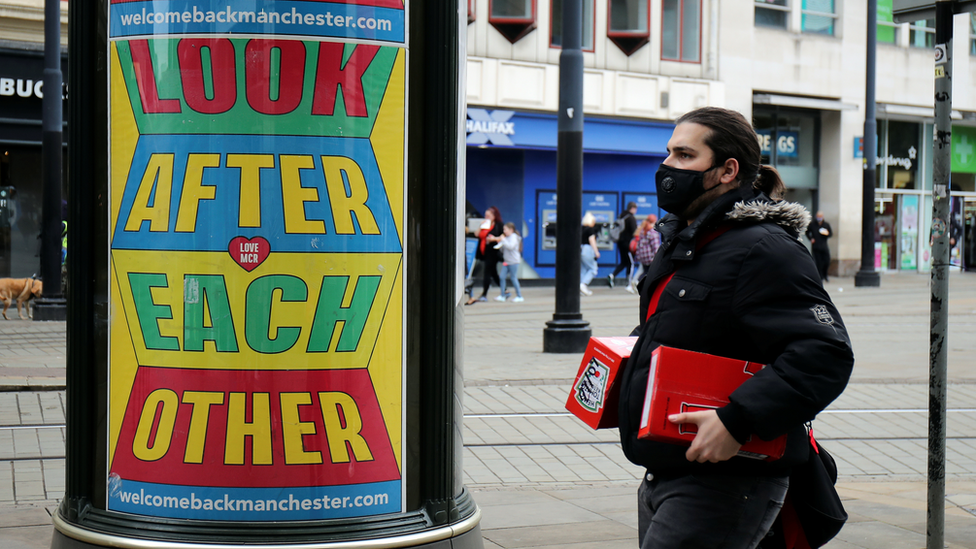 person in facemask walks past look after each other sign