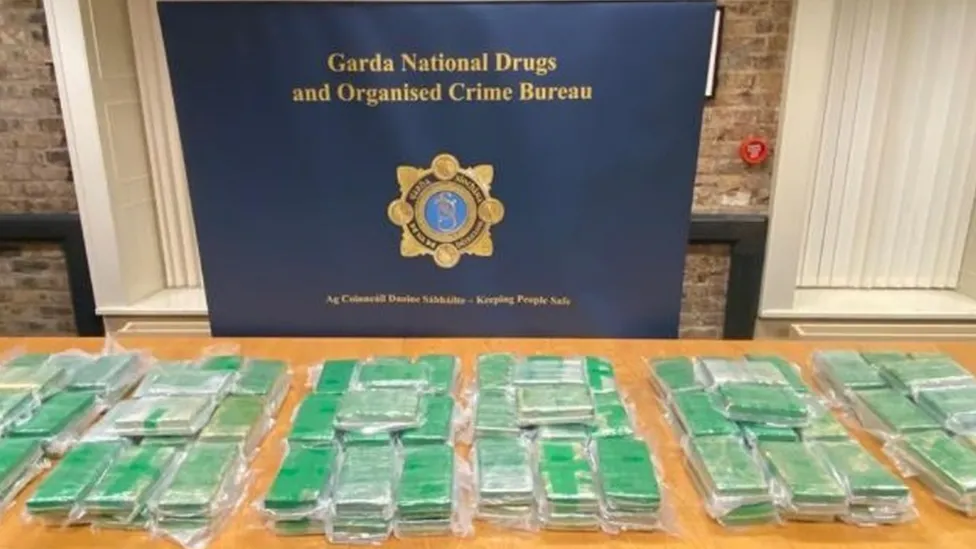 Six Green cocaine parcels, laid out on a wooden table with a Garda Natiional Drugs banner and badge displayed in background